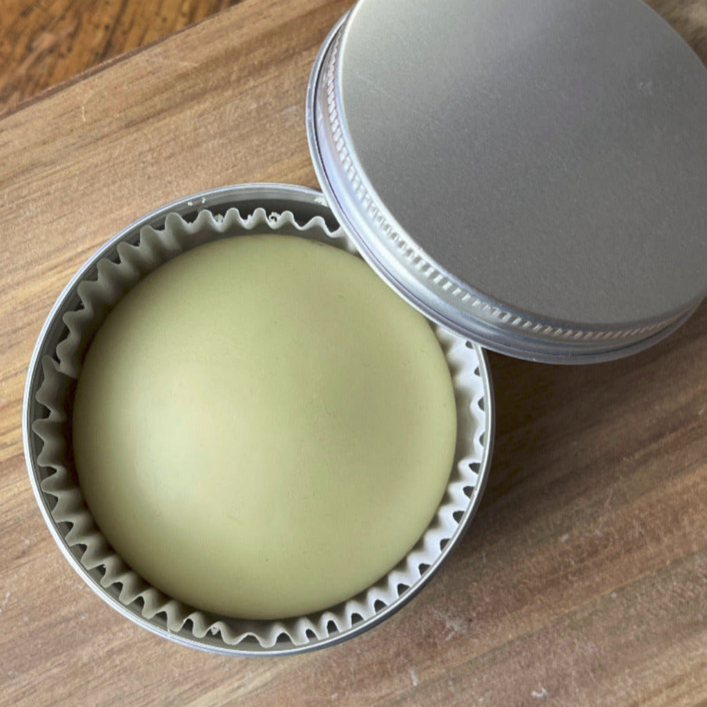A lotion bar in the shape of a stone inside a reusable tin container