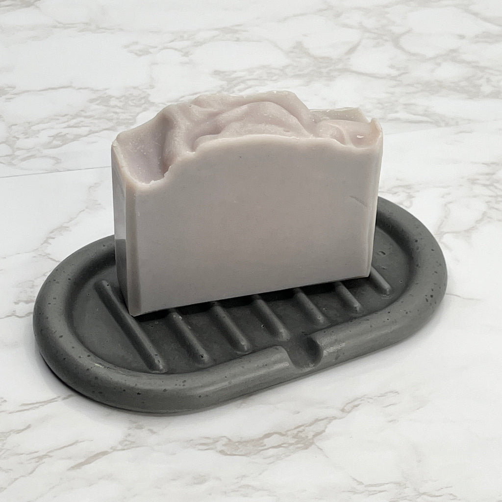 Handpoured self draining concrete soap dish in grey color with a soap bar showing size.