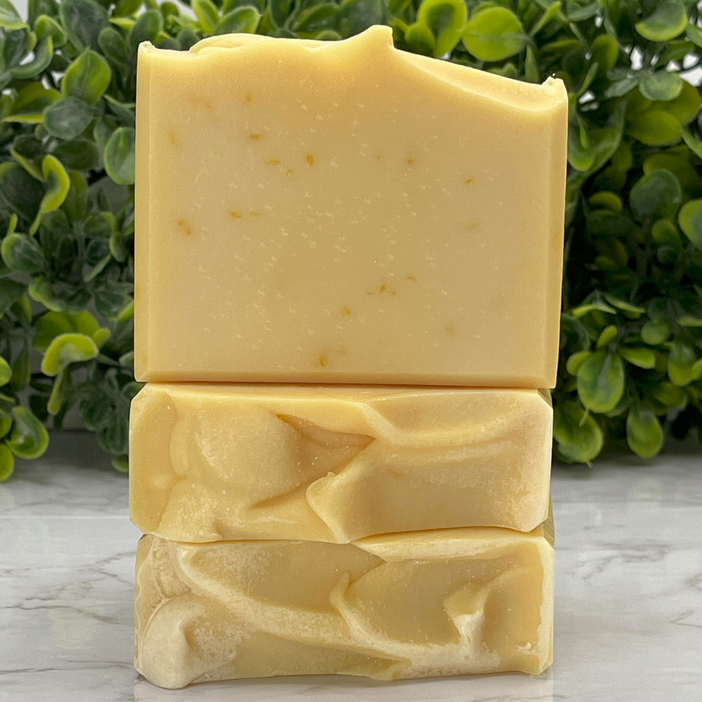 Three Lavender and lemongrass ocean water soap bars on a marble table with greenery in the background.