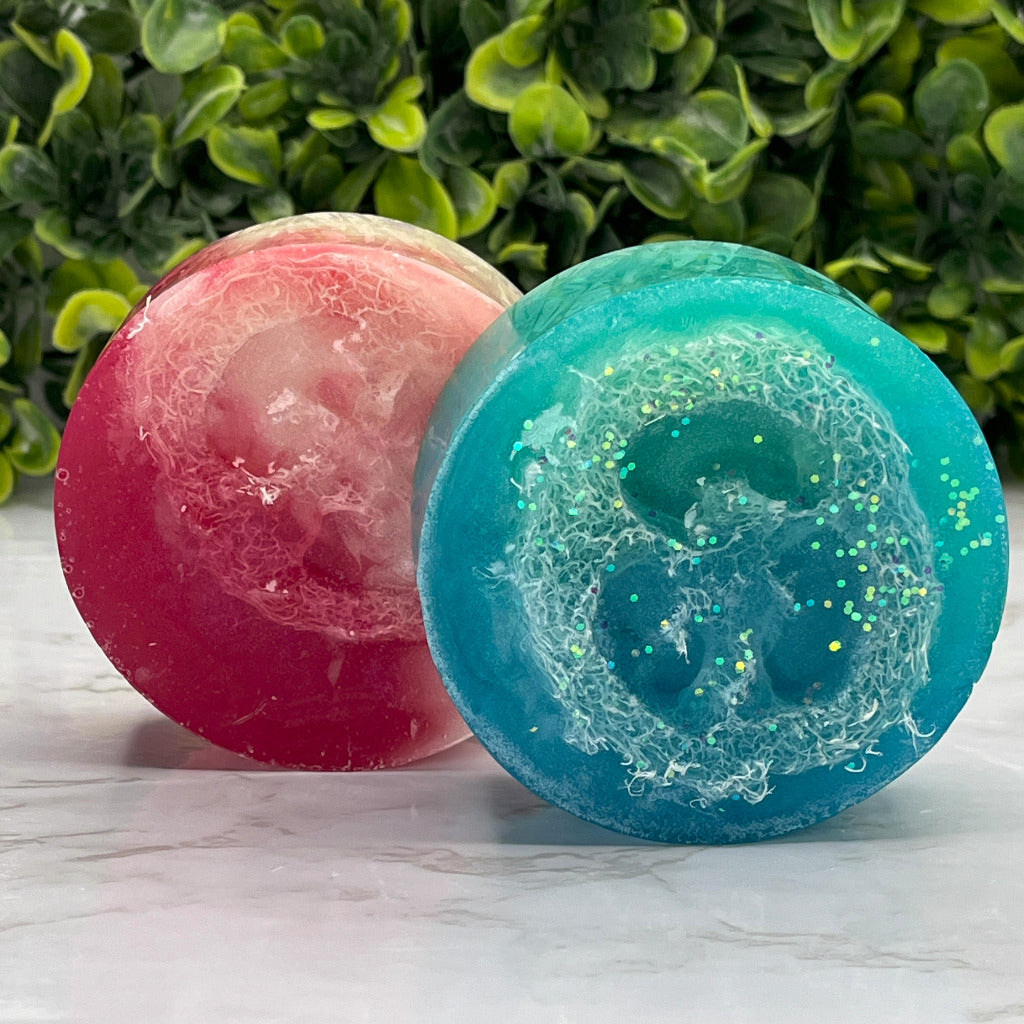 Two round soaps containing a section of a natural loofah for exfoliation.