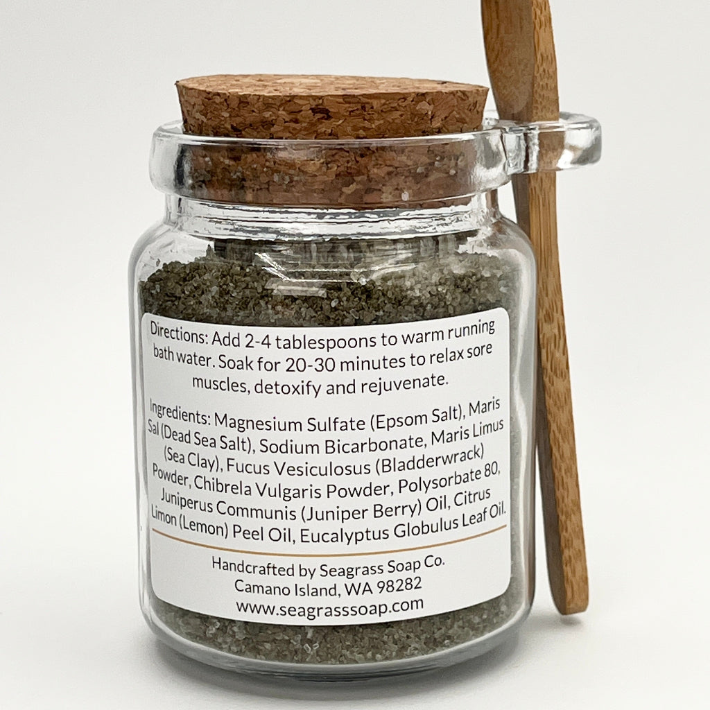 Glass jar with back label containing bath salts, wooden spoon on a white background