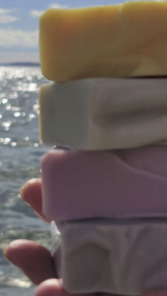 A hand holding 4 soap bars with the ocean in the background.