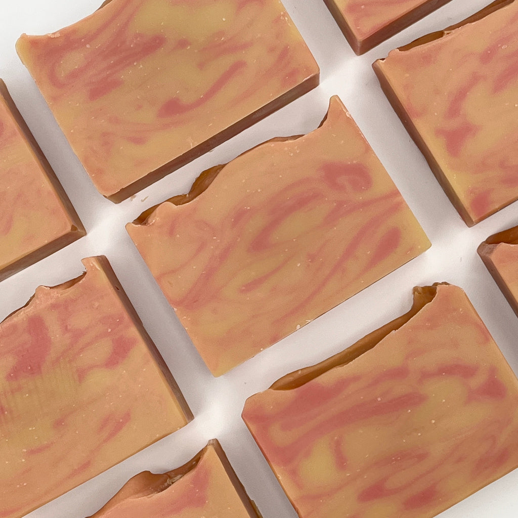 Multiple bars of Saratoga Sunset soap bars with orange and gold swirls on a white surface.