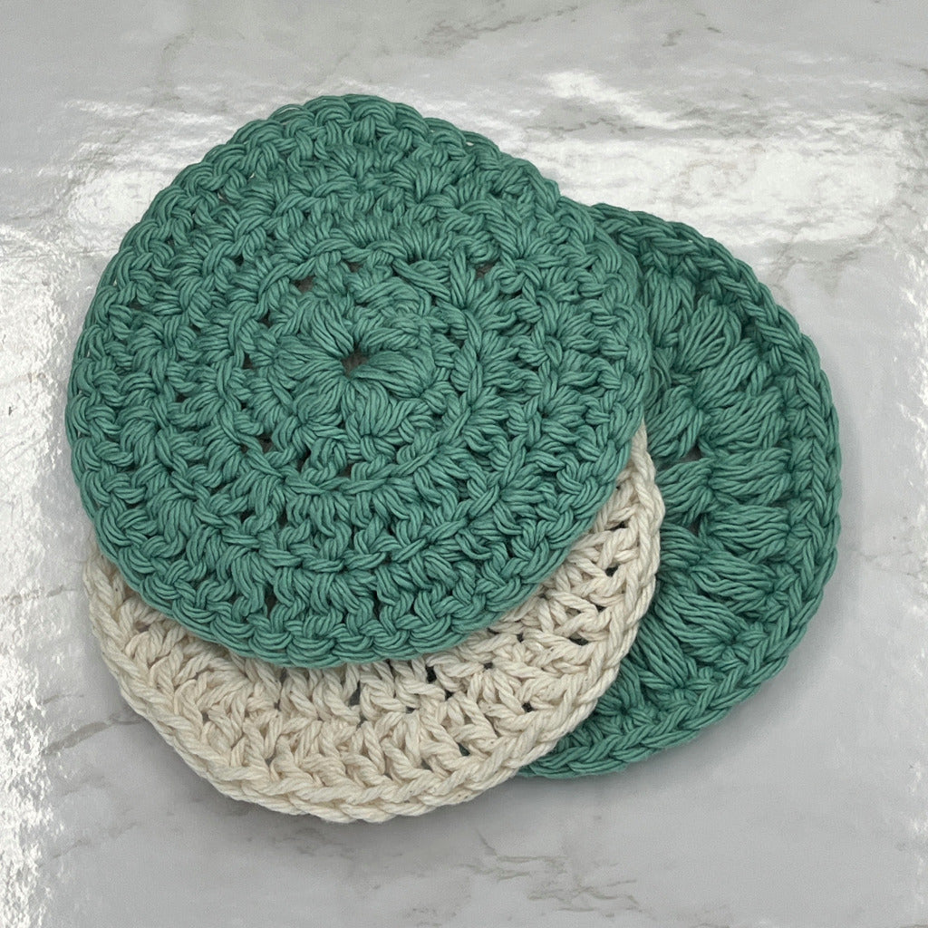 Set of three face cleansing round scrubbies in solid green and one solid cream color.