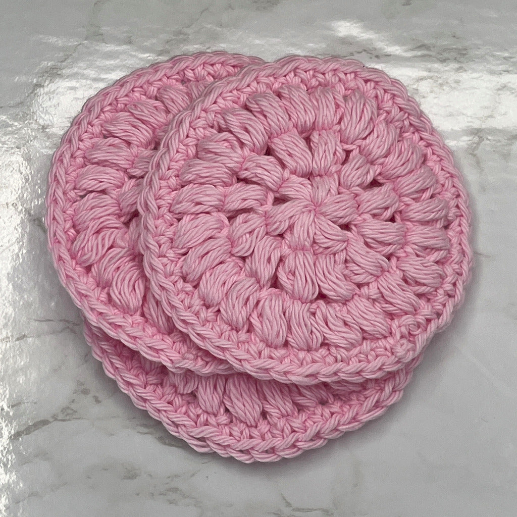 Set of three face cleansing round scrubbies in solid pink color.