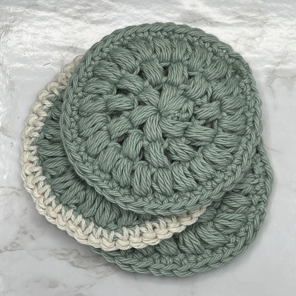 Set of three face cleansing round scrubbies in solid sage color and one in sage with a cream border.