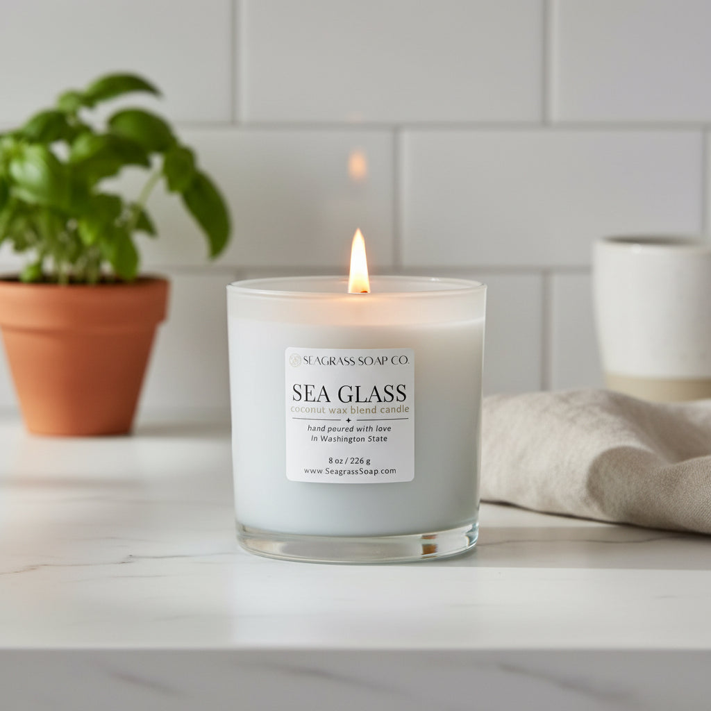 Sea Glass candle from Seagrass Soap Co sitting on a marble kitchen counter next to a beige towel and a basil plant in the background.