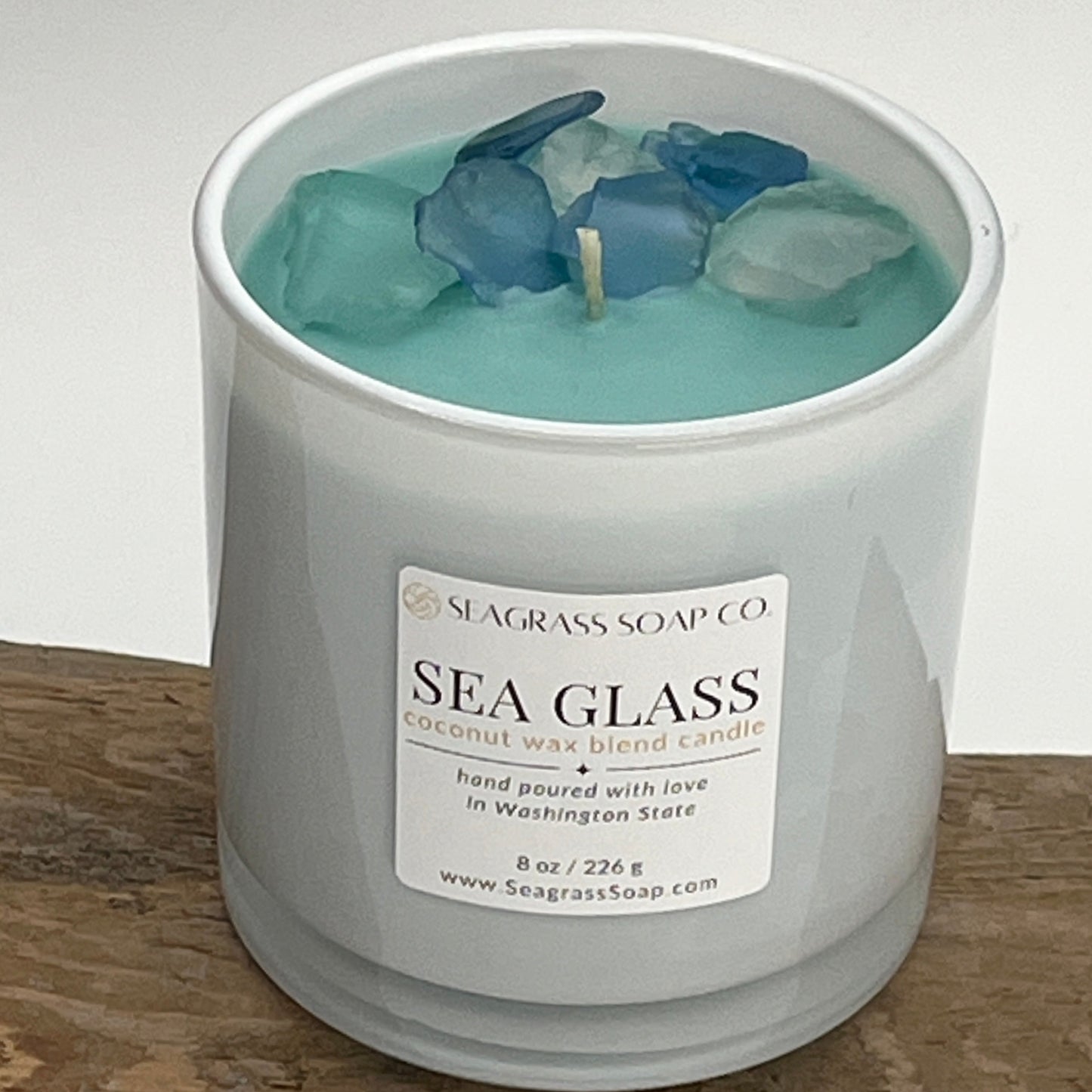 Sea Glass candle from Seagrass Soap Co. with aqua wax and seagrass on top sitting on driftwood.