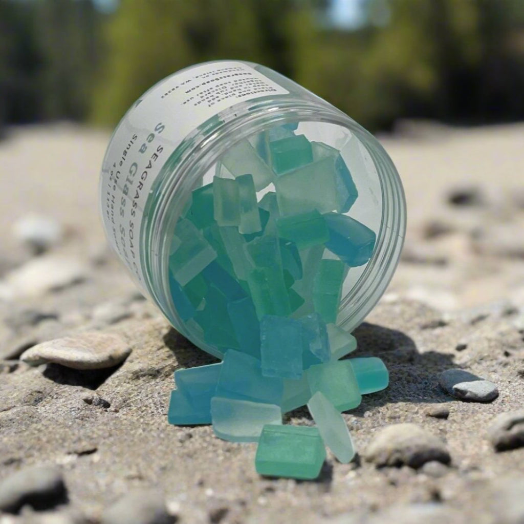 A jar of faux seaglass individual hand soaps laying on a beach.