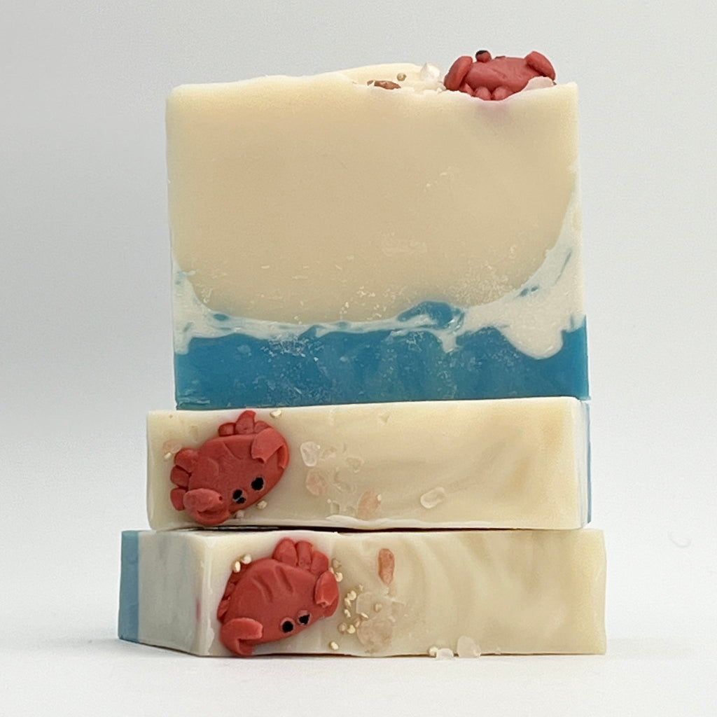 Three Tide Pool soap bars showing a beach scene and adorned with a handmade crab soap on top on a white background