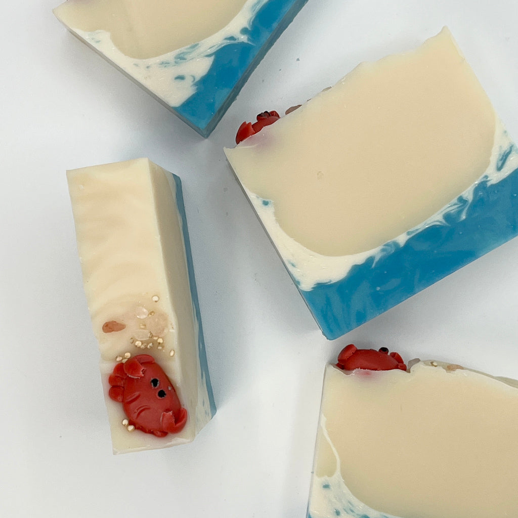 Four Tide Pool soap bar sshowing a beach theme adorned with a cute handmade crab soap sitting on top on a white surface.