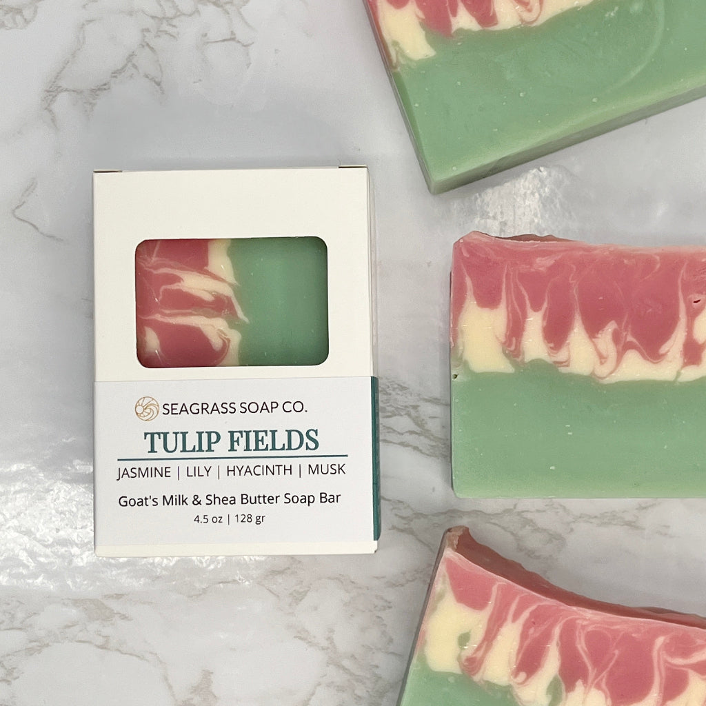 Three bars of Tulip Fields soap bars on a marbled surface laying next to box packaging.