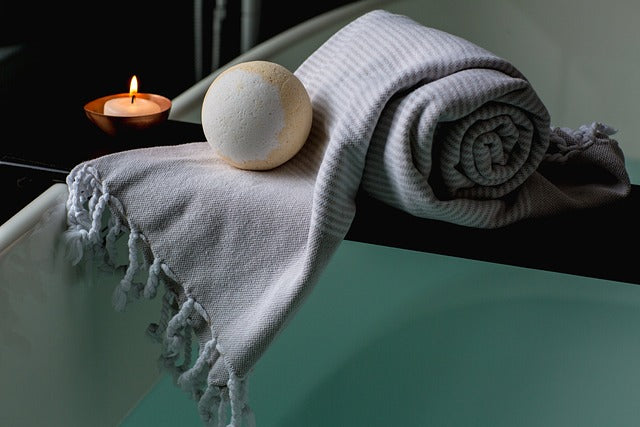 Bath bomb, candle and blanket sitting on a bathtub tray over a tub filled with water