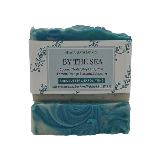 A rectangular bar of soap depicting a shoreline theme sitting on top of another bar showing the soap top design. Swirls of white and blue resemble the ocean and the tan colored sand contains ground coffee for a light exfoliation.