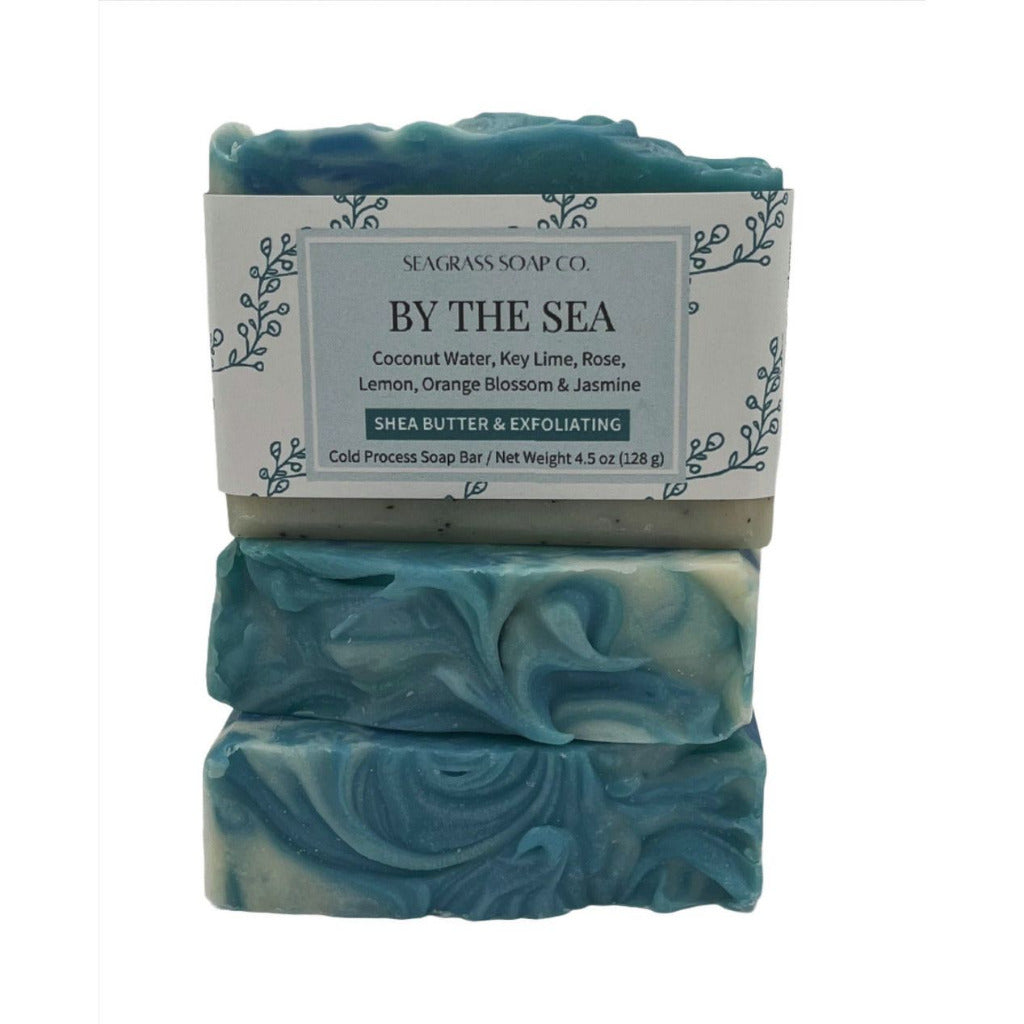 One bar of soap with label sitting on top of two bars of soap showing the top design. The theme of the soap is of a shoreline with white and light blue swirls and a sandy beach with coffee grounds for a light exfoliation.