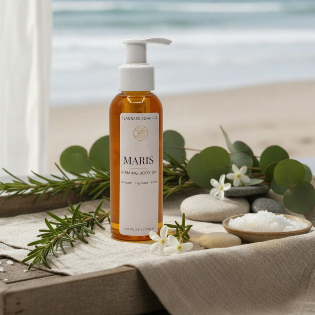 Maris firming golden body oil by Seagrass Soap Co. on a linen cloth with greenery, stones, and sea salt, set against a soft beach background.