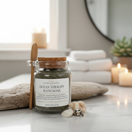 A jar of ocean therapy bath soak by Seagrass Soap Co. with seashells, towels, candles  and driftwood in the background.