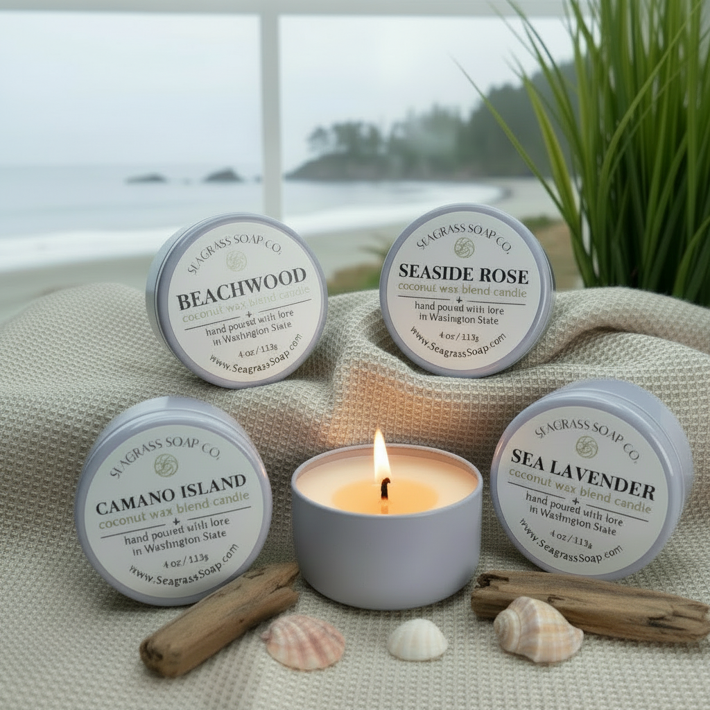 A variety of Sea Grass Soap Co. candles with visible labels on a textured surface with greenery in the background with a coastal view out a window.