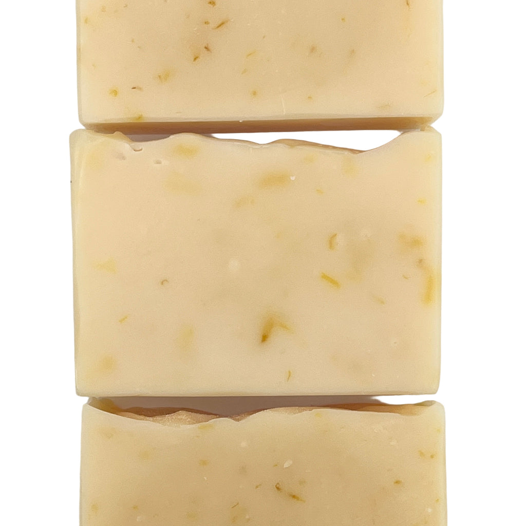 Three bars of light golden colored soap with specks of calendula petals 
on a white background