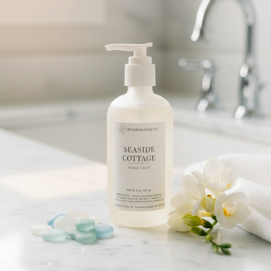 Hand soap bottle labeled 'Beach Glass' on a white surface surrounded by beach glass and florals next to a sink