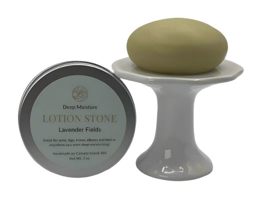 A lotion stone on a pedestal next to a tin container with lavender buds laying in the foreground