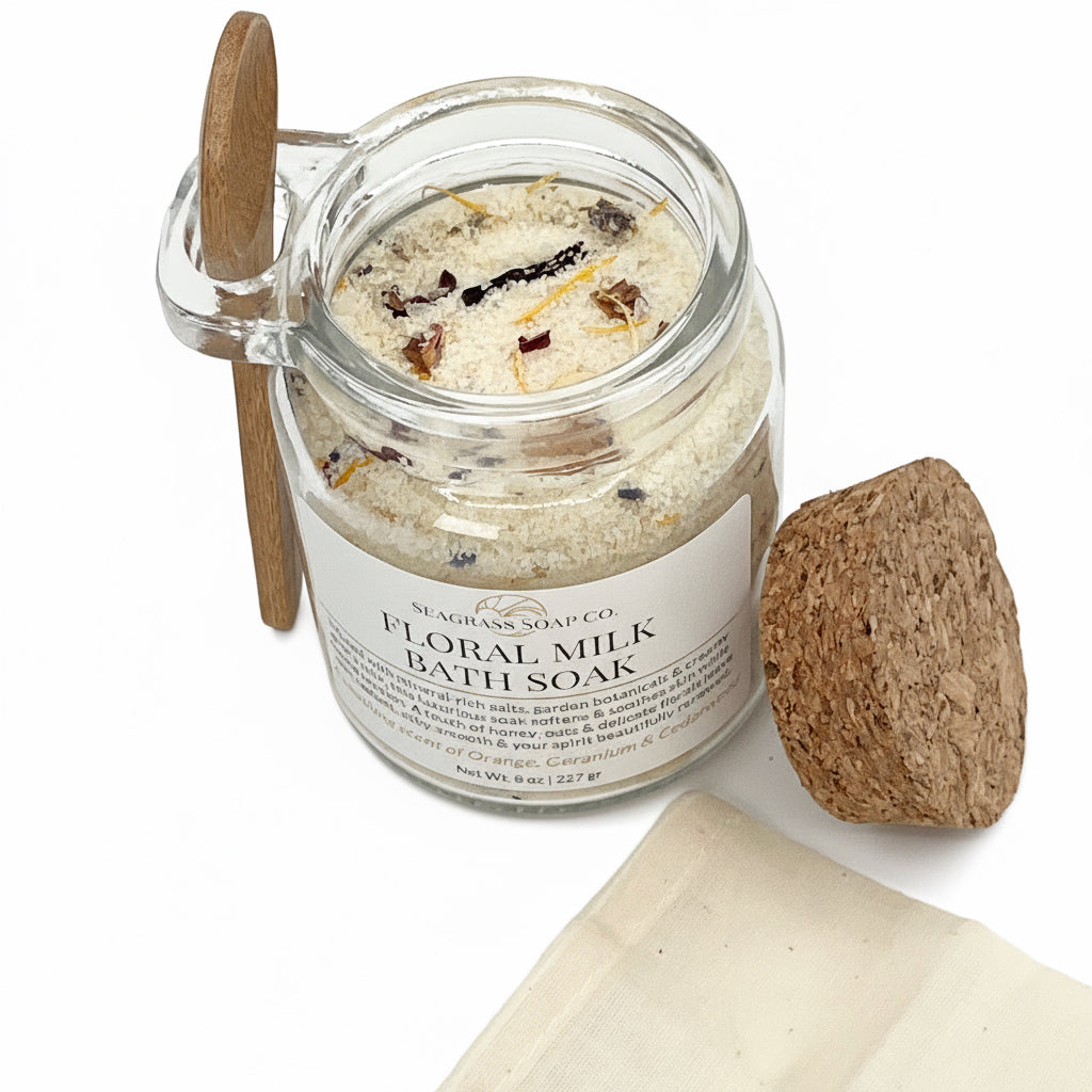 Jar of floral milk bath soak with a wooden scoop, cork lid and a tea bag on a white background