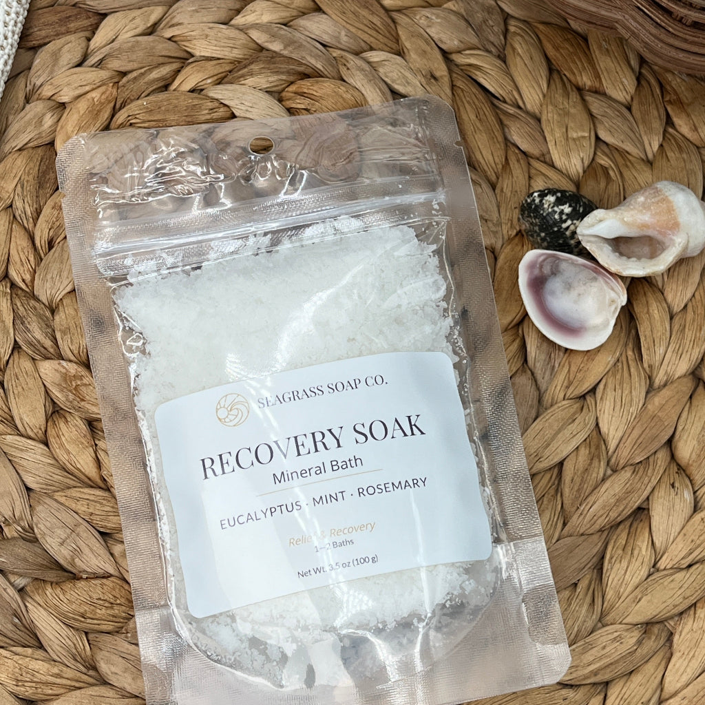 Package of muscle recovery mineral bath salts on a woven mat with shells and a starfish.