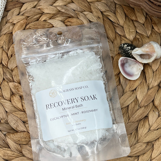 Package of muscle recovery mineral bath salts on a woven mat with shells and a starfish.