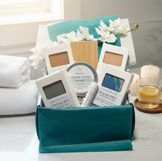 Gift box with four bars of soap, a wooden soap saver, a lotion stone and a lip balm styled on a table with bath accessories