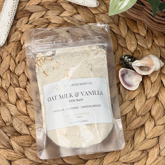 Packaged of oat milk and vanilla milk bath soak product on a woven surface with starfish and shells.