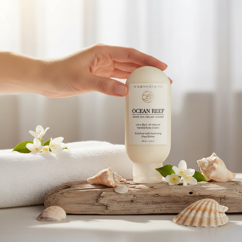 All natural hand and body cream enriched with Shea Butter, scented in Ocean Reef by Seagrass Soap Co sitting on a piece of driftwood next to a towel and sea shells
