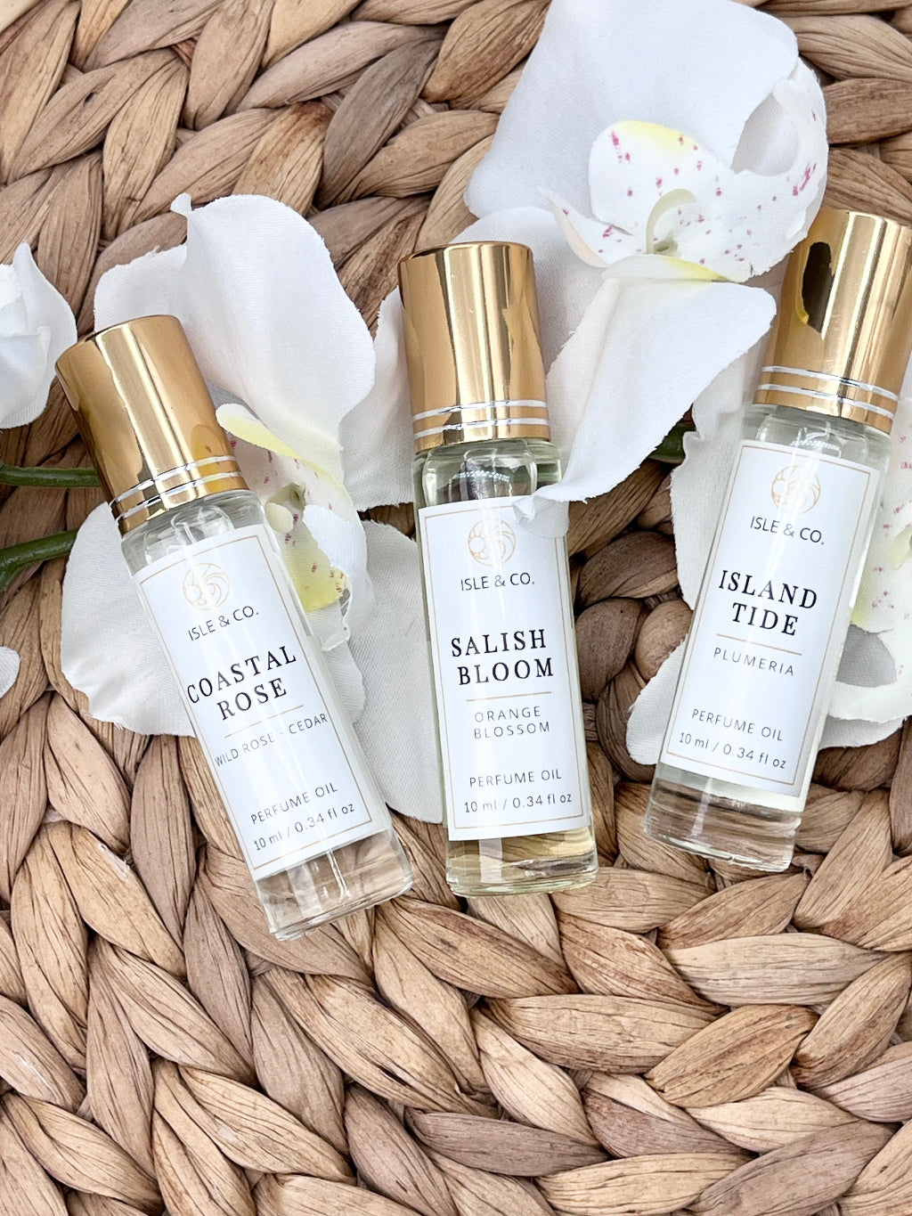 Three perfume bottles labeled 'Coastal Rose', 'Salish Bloom', and 'Island Tide' on a woven surface.