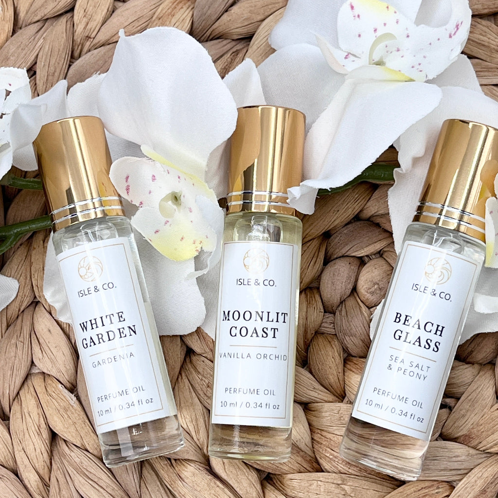 Three perfume bottles labeled 'White Garden', 'Moonlit Coast', and 'Beach Glass' on a woven surface.