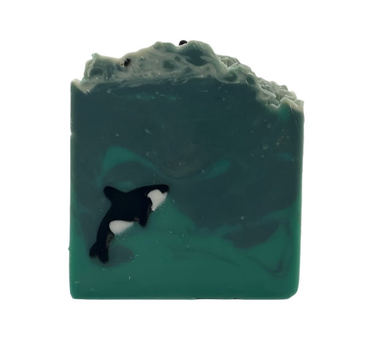 A handmade orca embedded in a soap bar swimming in the Salish Sea of green and blue swirls.