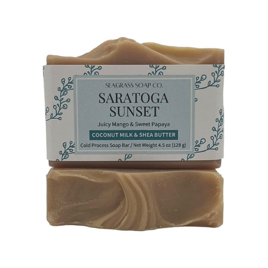 A close up view of two bars of soap with a light tan color, one bar displays the label and the other shows the soaps top design.