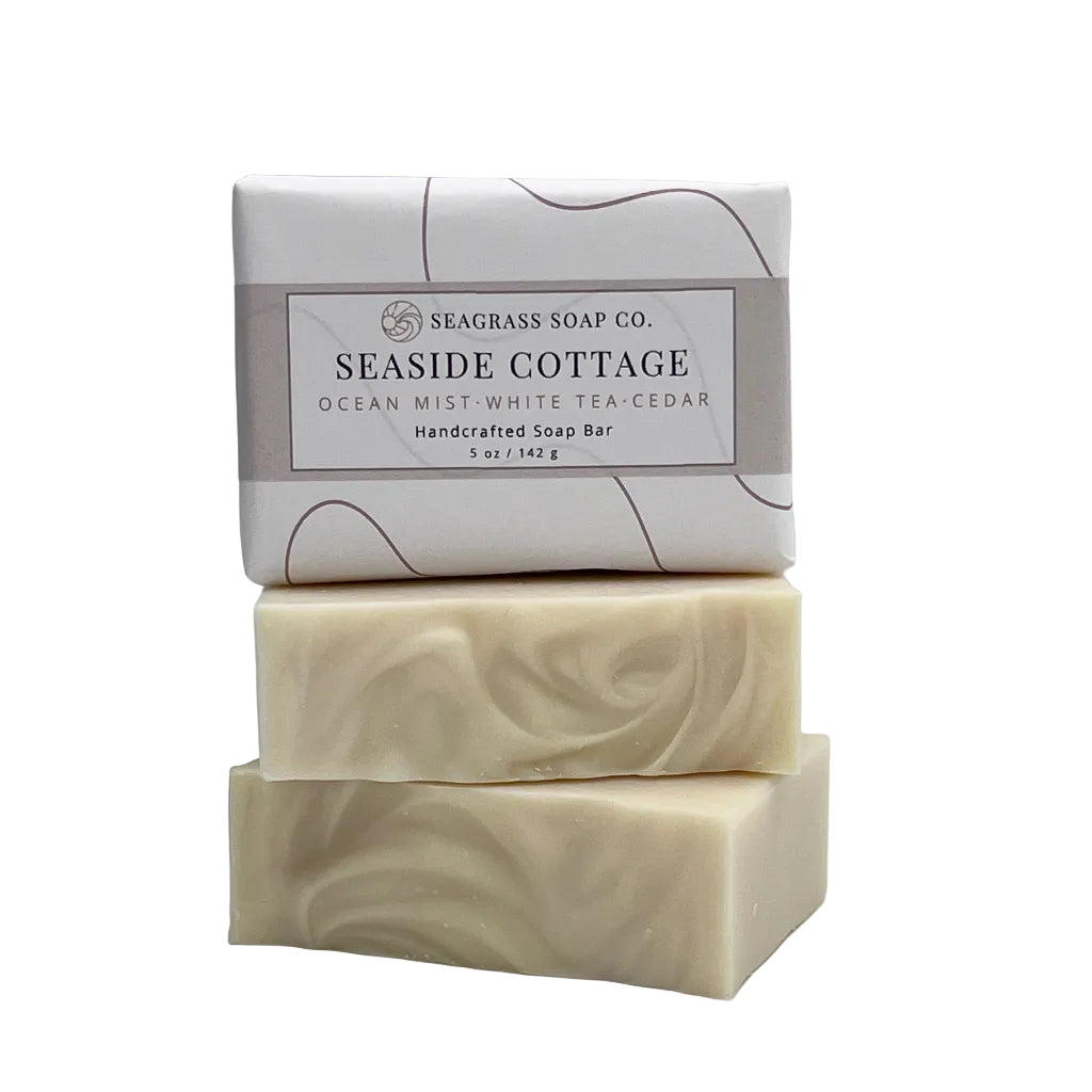 Three stacked Seaglass Soap Co. 'Seaside Cottage' ocean mist white tea cedar handcrafted soap bars, with the top bar wrapped in a white paper label, on a white background.