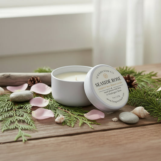 Seaside Rose candle in a white tin sitting on a wooden bench surrounded by rose petals, driftwood and everygreen branches by Seagrass Soap Co