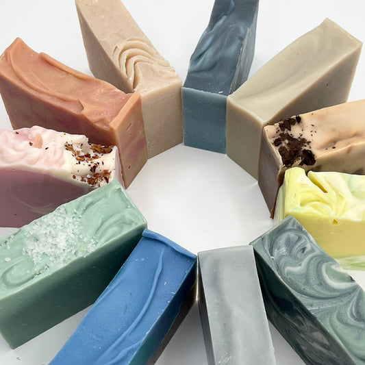 Assorted bars of soap in various colors and textures arranged in a circular pattern on a white background.