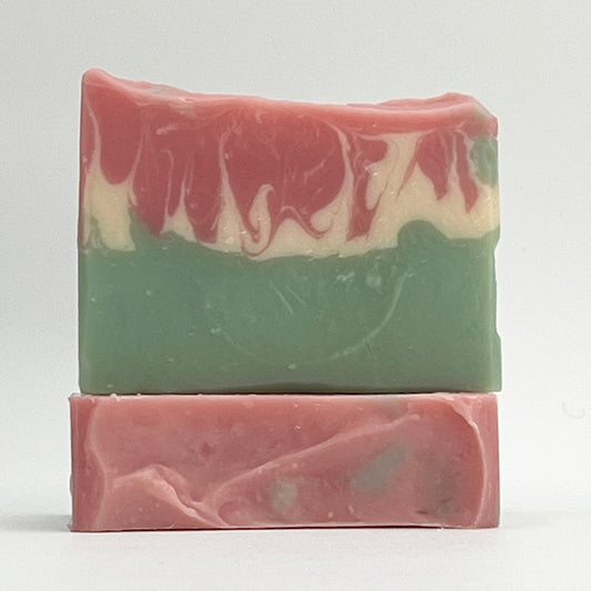Two bars of our goat milk and shea butter Tulip Fields soap bars with a green base and a pink and white design on top on a white background.