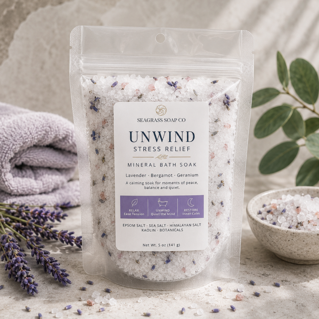 Unwind mineral bath soak package displayed with lavender and botanical accents on a neutral stone surface.