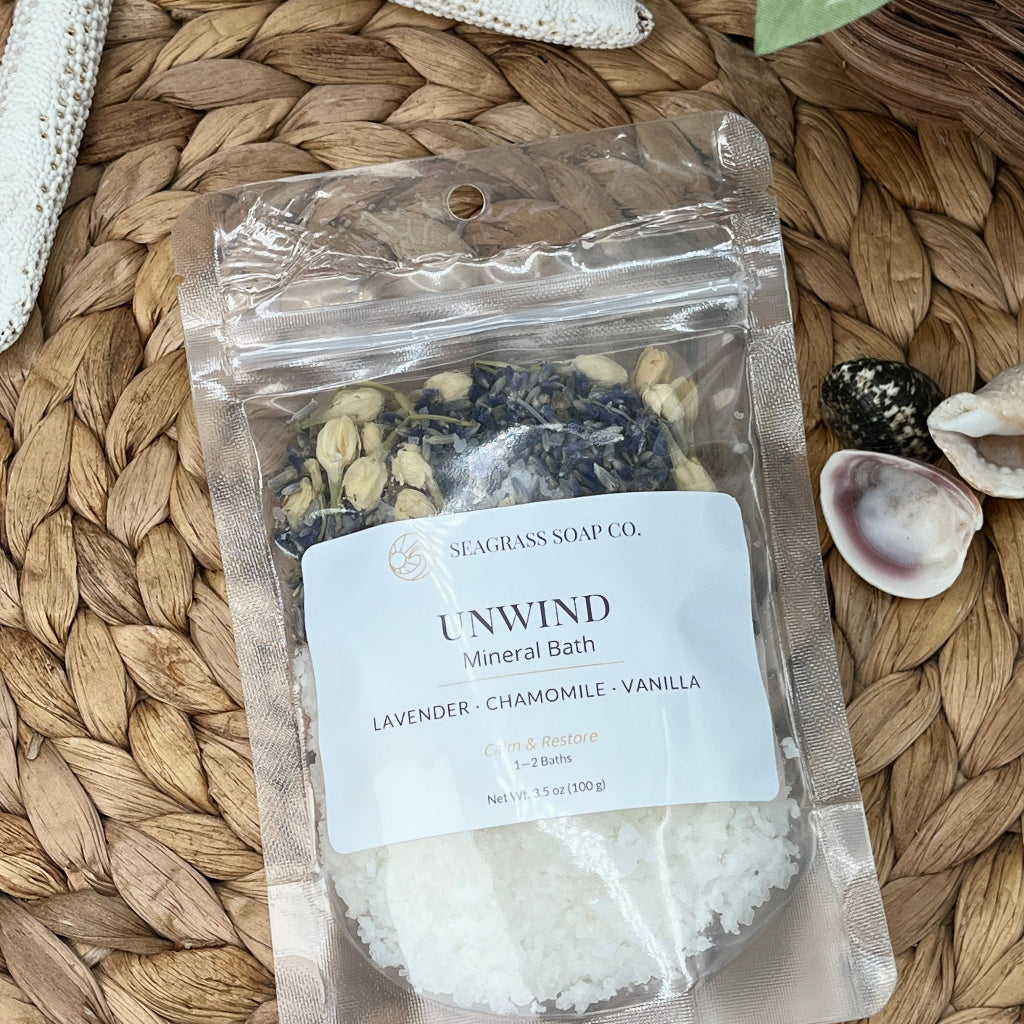 Unwind mineral bath salts package on a woven mat with starfish and shells.
